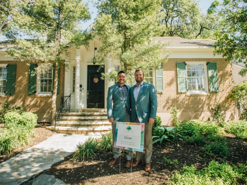 Gay couple standing by sold sign in front of their new home in Austin, TX