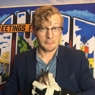 Travis, a parent looking to adopt a baby, holding an armadillo in front of an Austin sign